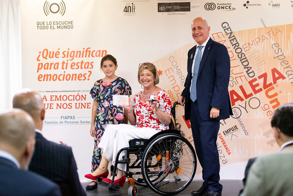 Mujer en silla de ruedas con el premio, acompañada de una niña y un hombre.